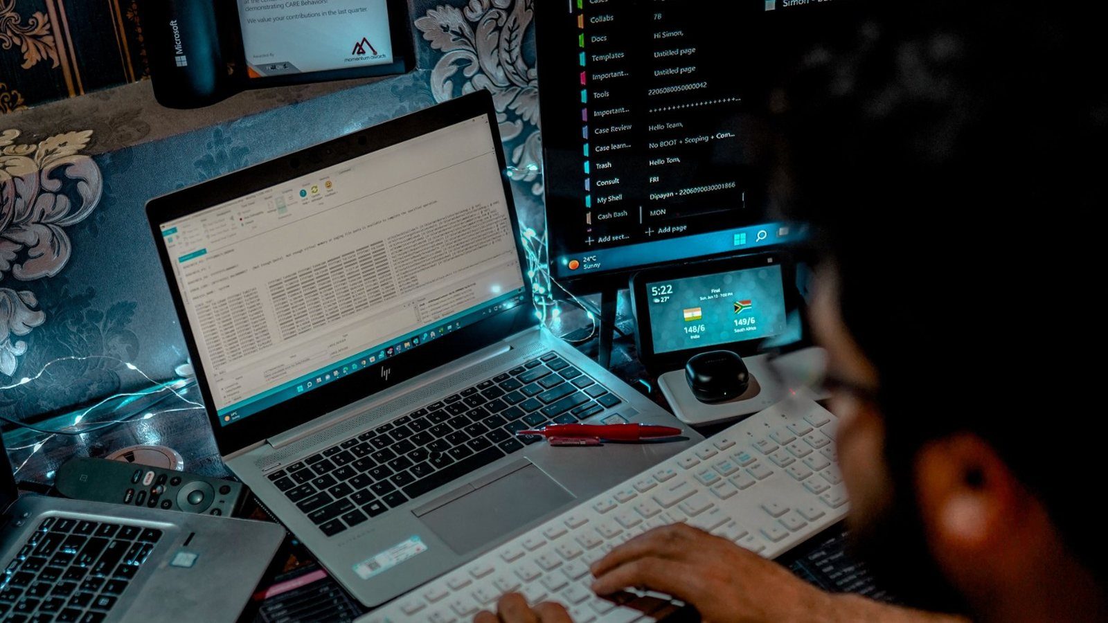 An IT professional working across two laptops and a monitor full of case notes