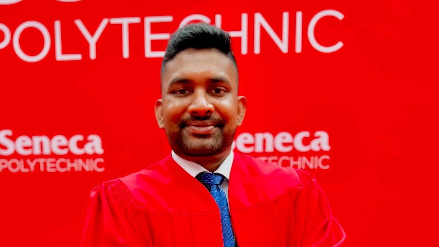 Yuvin Walker in a red convocation gown at Seneca Polytechnic, arms crossed, facing the camera
